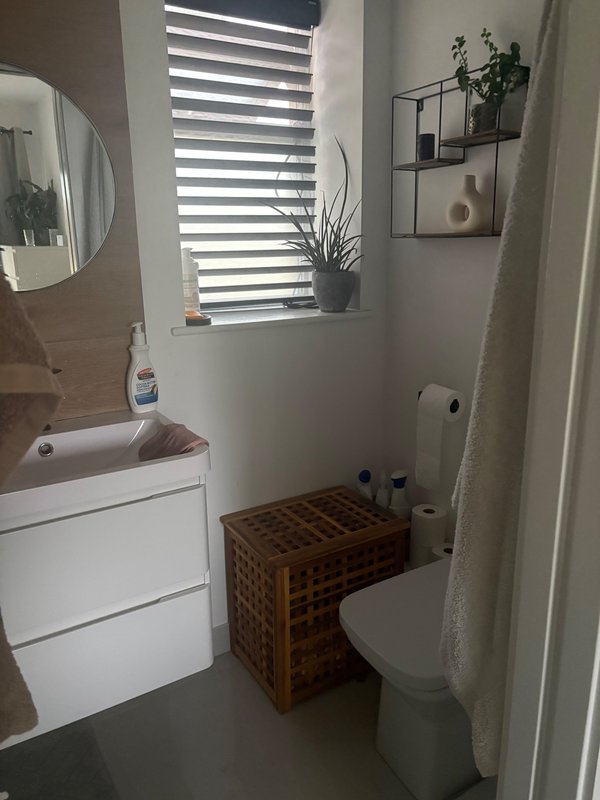 Compact bathroom with white sink, toilet, mirror, window with blinds and woven storage