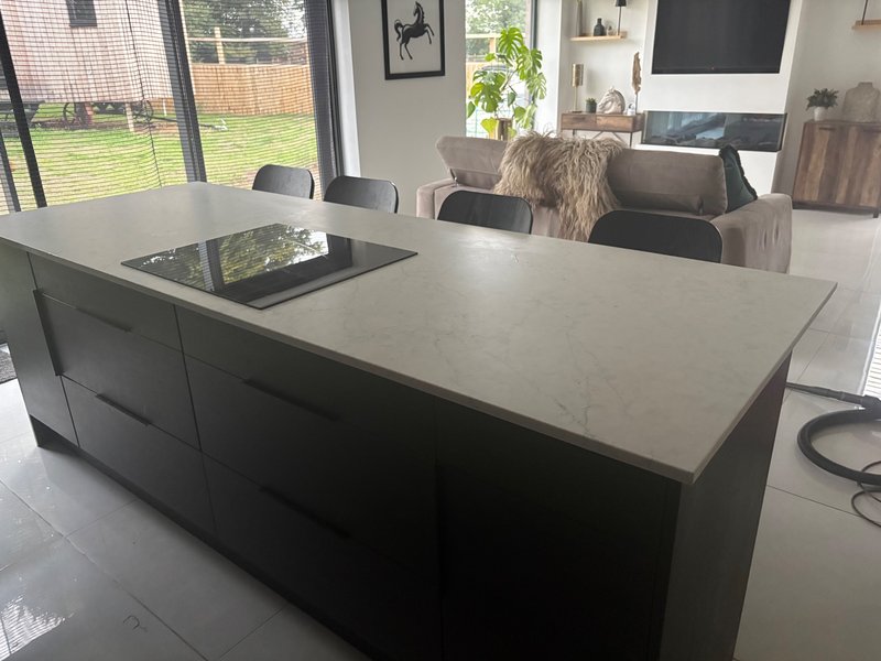 Modern kitchen with large island, white countertop, black base units and garden view