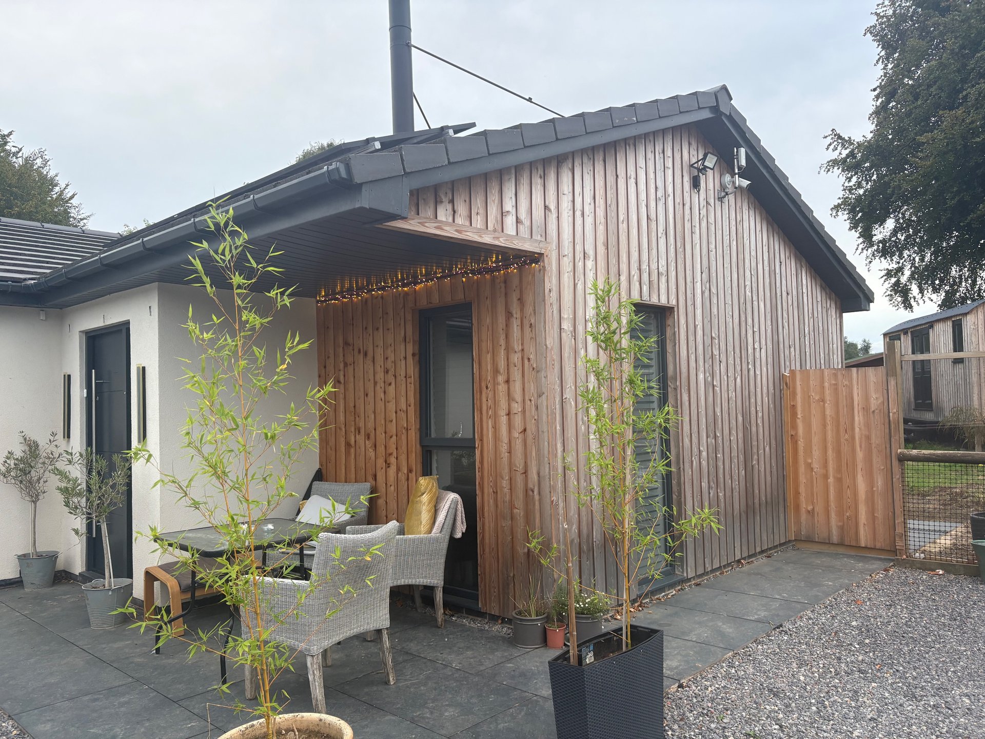 Modern wooden cabin with covered patio, seating area, and landscaped garden entrance