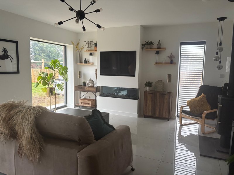 Modern living room with brown sofa, wall-mounted TV, plants, and glass doors to garden