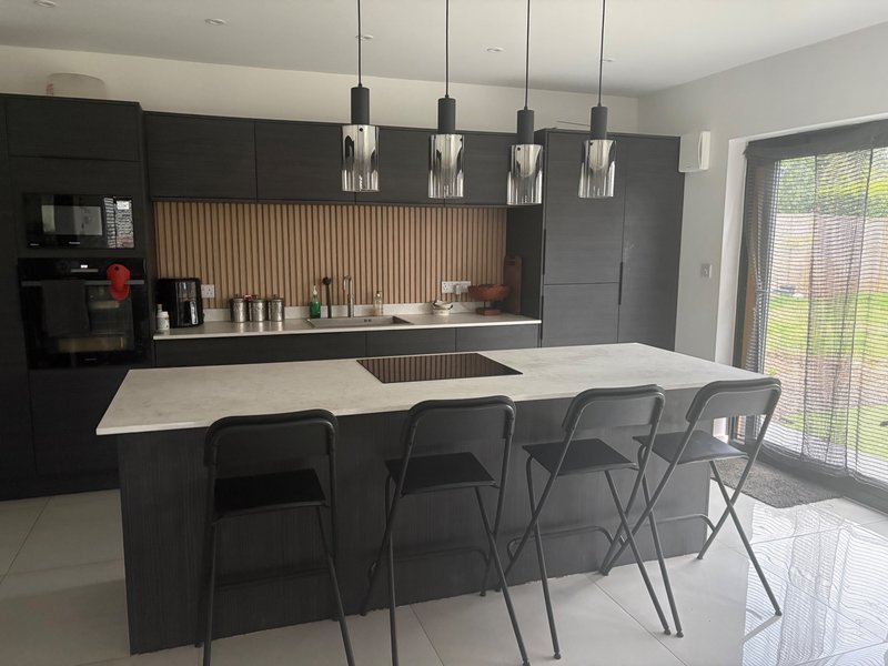 Modern kitchen with dark cabinetry, white island, bar seating, and pendant lights