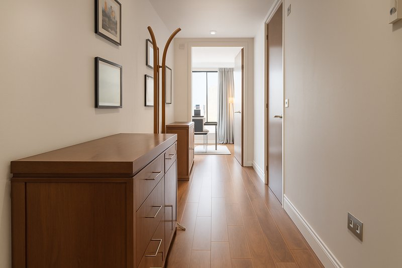 Neutral hallway with wooden dresser, framed wall art, coat stand and view to living area