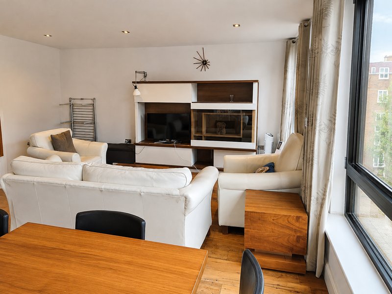 Modern living room with white sofa, wooden dining table, TV unit and large windows