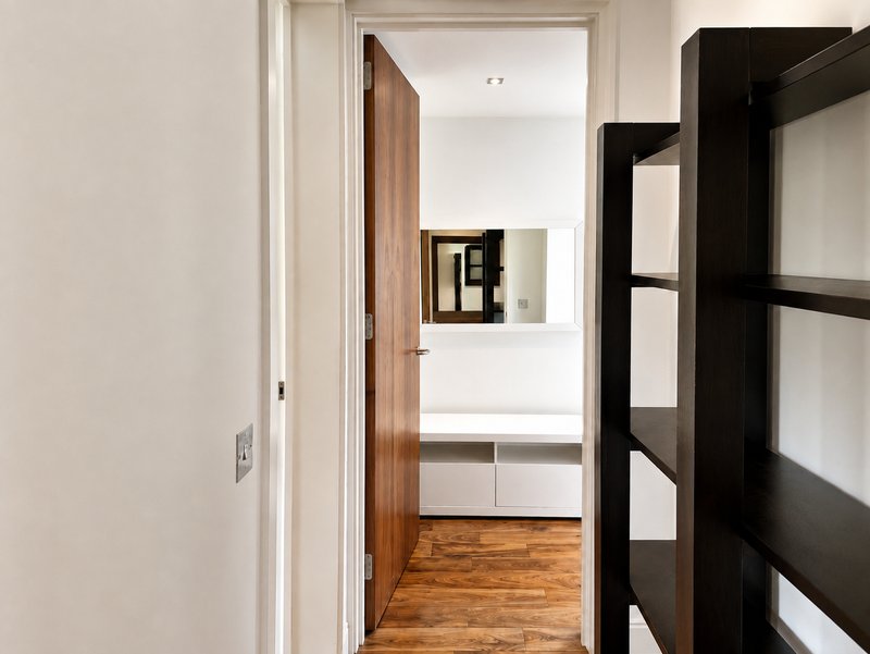 Hallway with wooden door, black shelving unit, and view into bright bathroom with vanity