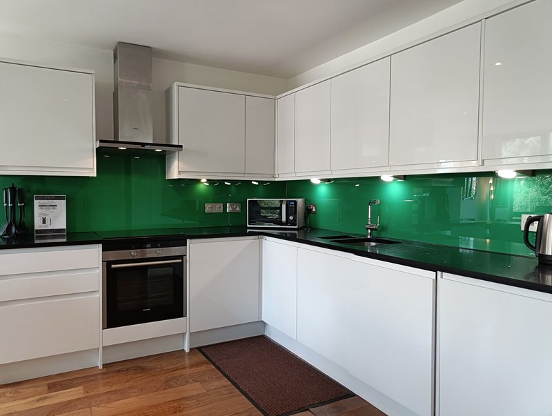 Modern kitchen with white cabinetry, green backsplash, black countertops and stainless steel appliances