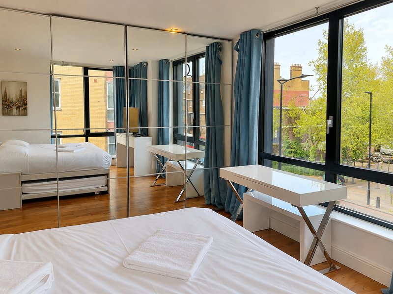 Modern bedroom with double bed, mirrored wardrobe, desk, and floor-to-ceiling windows overlooking trees