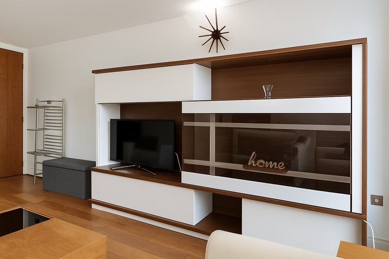 Modern living room with built-in wood and white shelving unit, flat-screen TV, and decorative wall clock