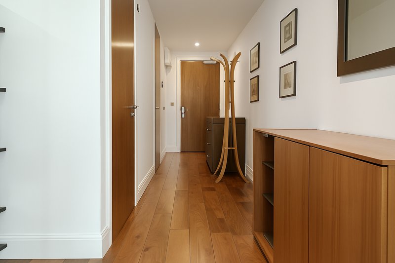 Bright hallway with wooden flooring, white walls, wood doors and framed artwork