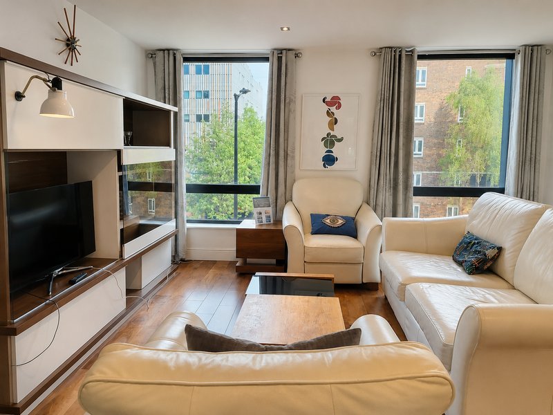 Modern living room with cream upholstered furniture, TV, wooden coffee table and large windows