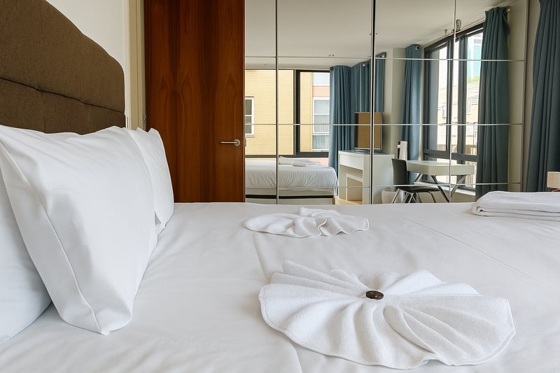 Modern bedroom with white bedding, brown headboard, mirrored wardrobe and blue curtains