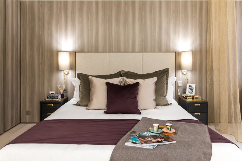 Modern bedroom with upholstered headboard, purple accent pillows, bedside lamps, and striped curtains