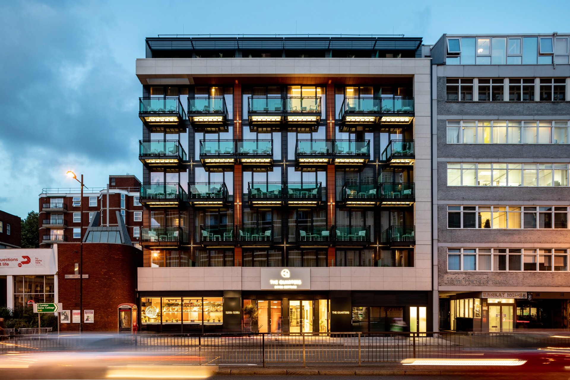 Modern multi-story residential building with glass balconies and mixed brick facade, street view at dusk
