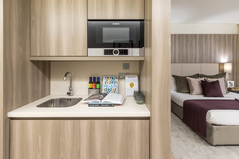 Studio kitchenette with sink, microwave, and workspace, adjacent to bedroom with double bed