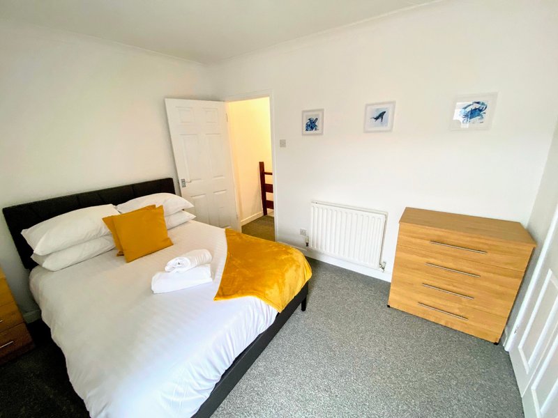 Bedroom with double bed, yellow bedding, wooden dresser, and white walls