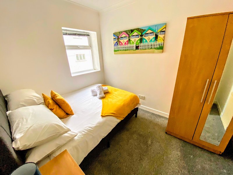 Compact bedroom with single bed, yellow cushions, wooden wardrobe and window