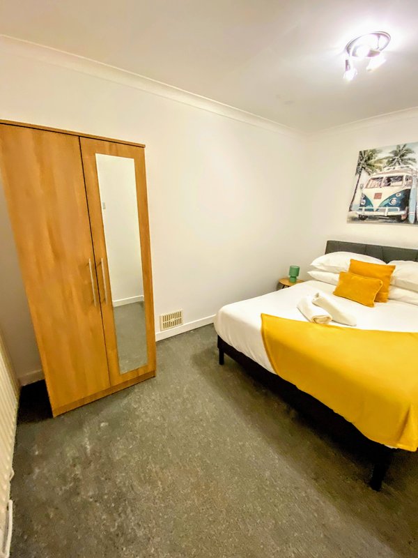 Bedroom with double bed, yellow bedding, wooden wardrobe, and wall art