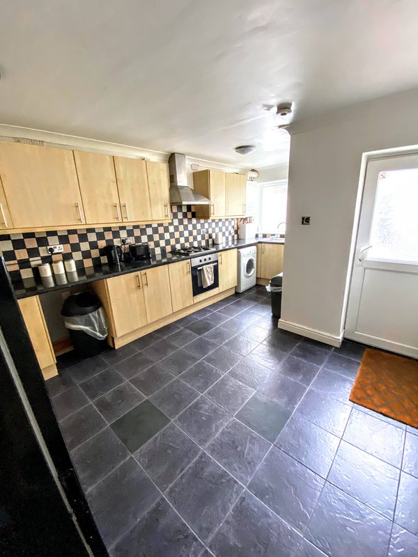 Kitchen with wooden cabinets, checkered backsplash, black tile flooring, and door to garden