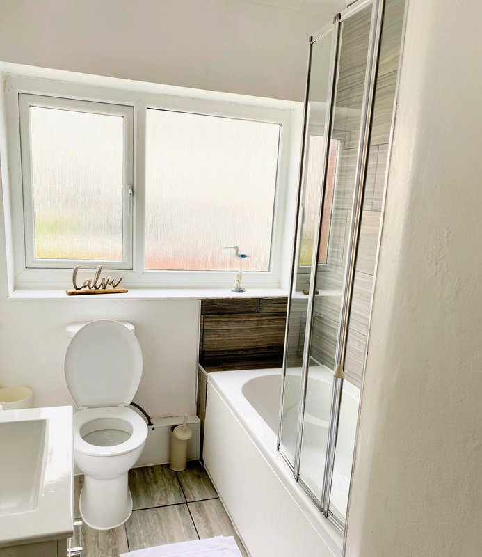 Bathroom with toilet, bathtub, shower screen, window and wooden flooring