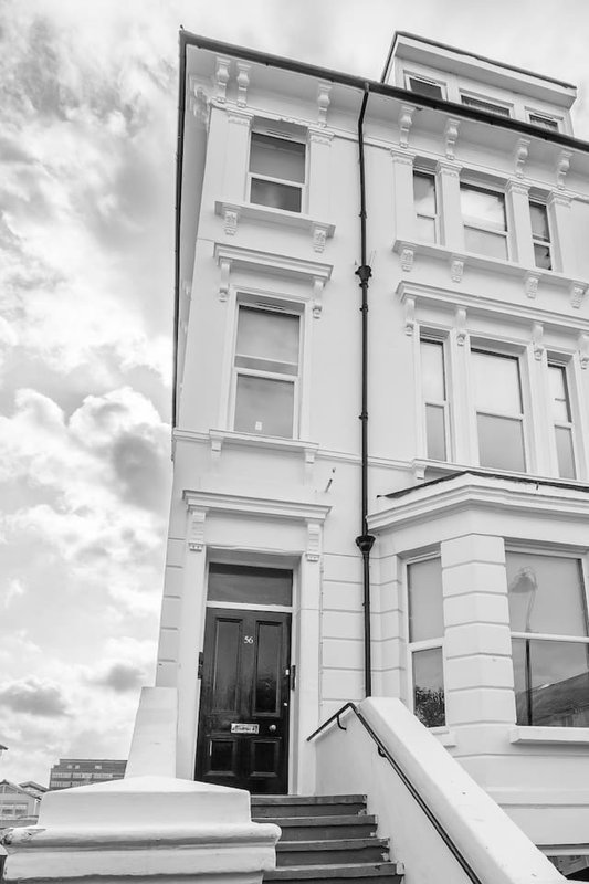 Black and white exterior of a white Victorian terraced building with multiple sash windows and entrance steps