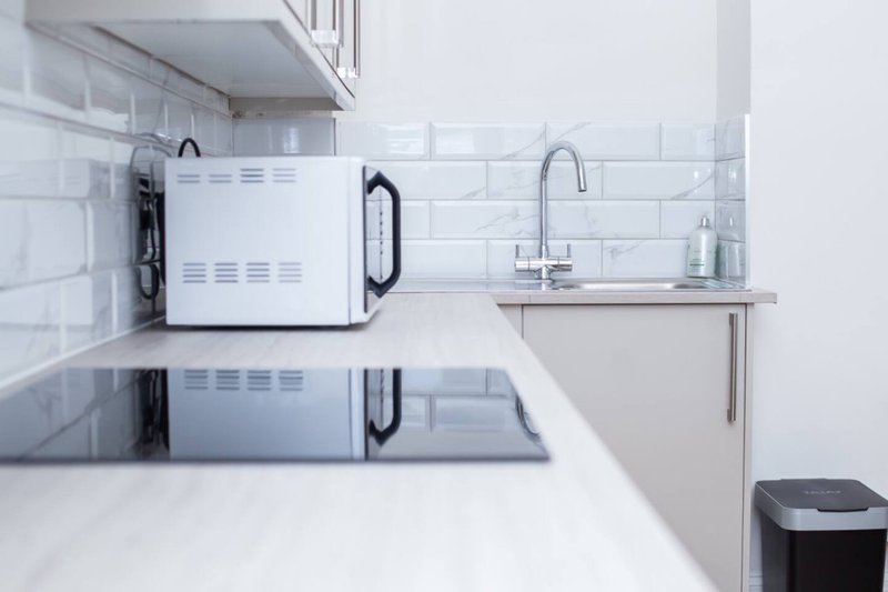 Modern kitchen countertop with white microwave, sink, tap, and subway tile backsplash
