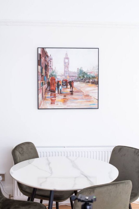 Dining area with white marble round table, grey upholstered chairs, and London street scene artwork