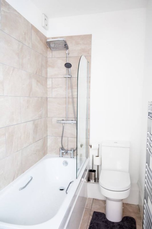 Modern bathroom with bathtub, shower head, toilet, and beige tile walls
