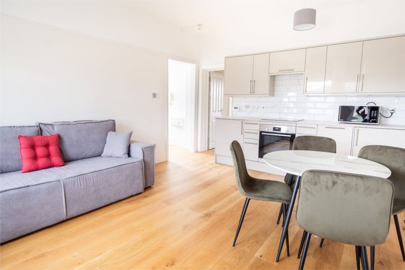 Open-plan living and kitchen area with gray sofa, dining table, and modern white cabinetry