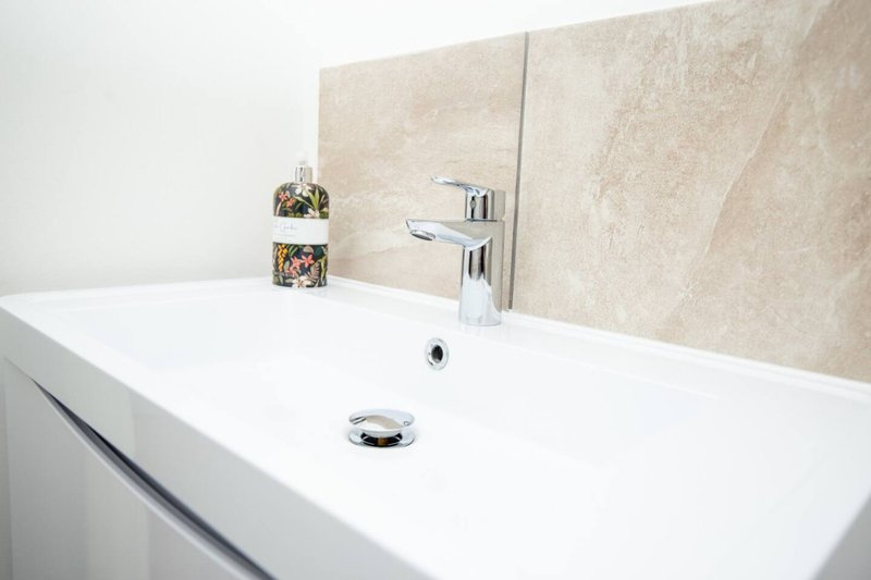 Modern bathroom sink with white countertop, chrome faucet, and beige tile backsplash