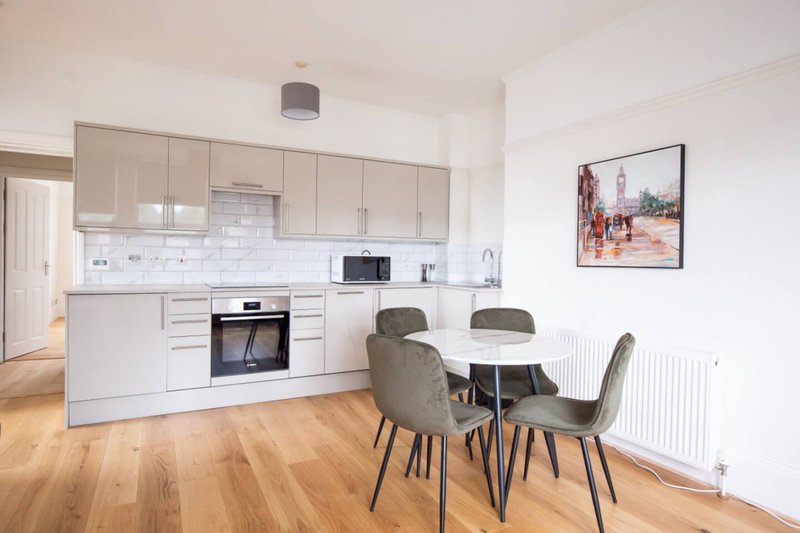 Modern open-plan kitchen and dining area with white cabinetry, wooden flooring, and round dining table