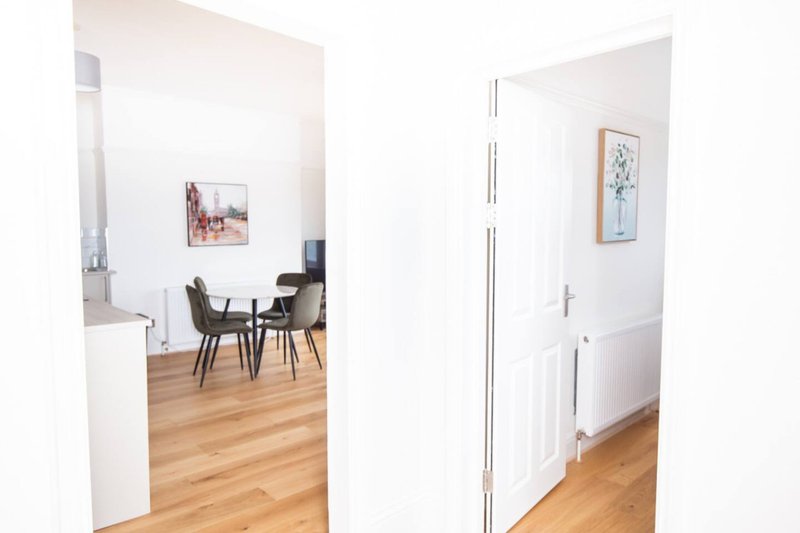 Open-plan living space with wooden flooring, dining area with chairs, and white walls with framed artwork