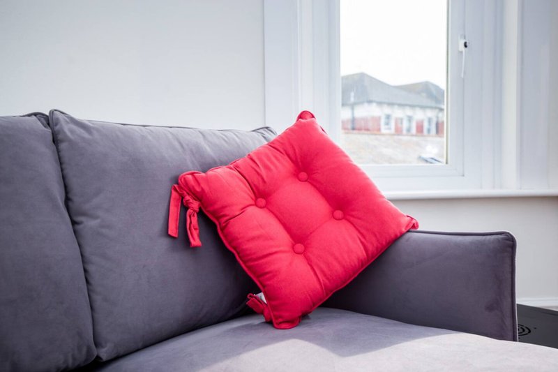 Gray sofa with red cushion and window overlooking residential street