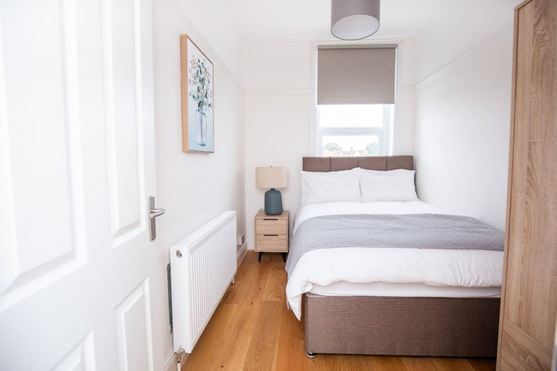 Compact bedroom with double bed, wooden floor, white walls and radiator