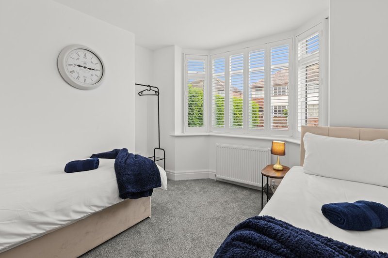 Bright twin bedroom with two beds, clock on wall, large bay window with shutters