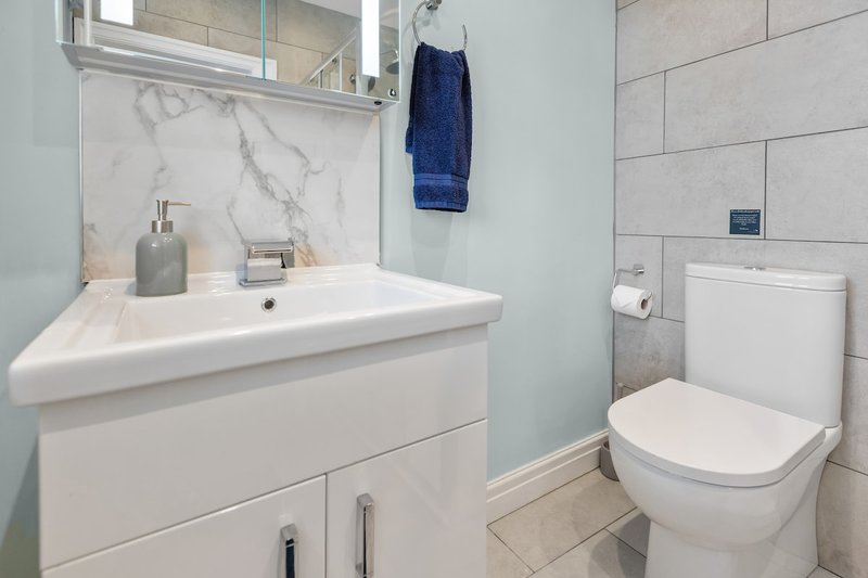Modern bathroom with white vanity sink, mirror, toilet, and blue towel hanging on wall