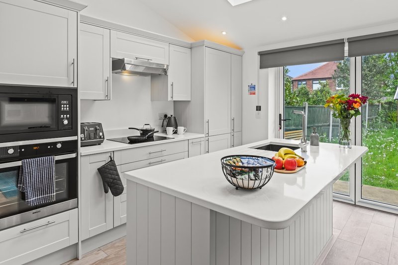 Modern white kitchen with island, built-in appliances, and garden view through patio doors