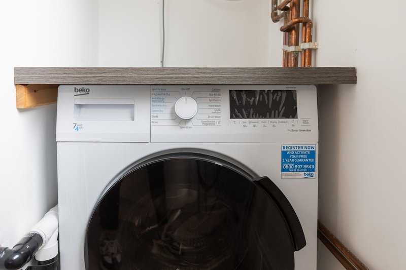 White front-load washing machine under wooden shelf with storage baskets