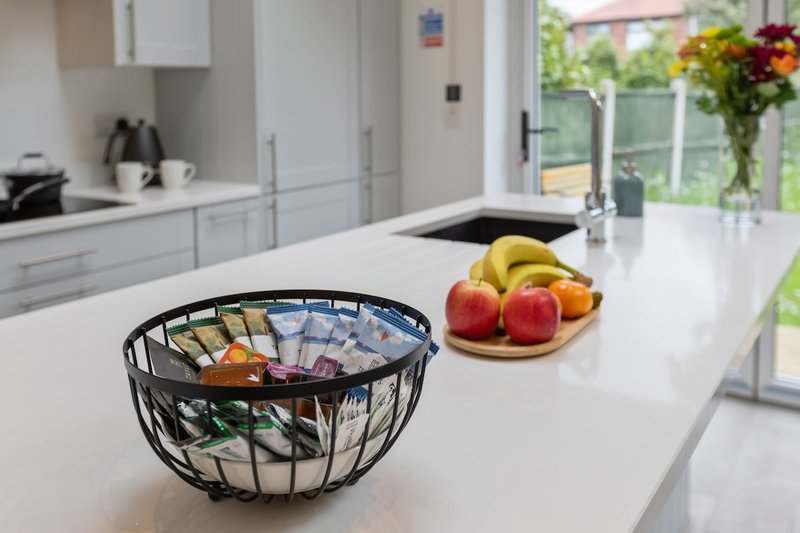 Modern kitchen with white cabinetry, island countertop, fruit bowls, and garden view