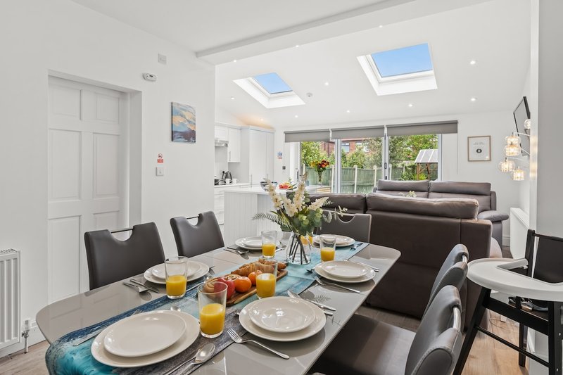 Open-plan living and dining area with skylight, set dining table, and dark sofa seating