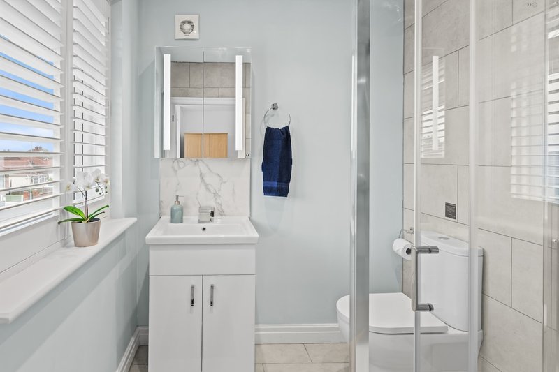 Modern bathroom with white vanity, mirror, toilet, and shower enclosure with tiled walls