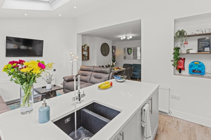 Modern open-plan kitchen with white countertop, sink, flowers in vase, and view to living area