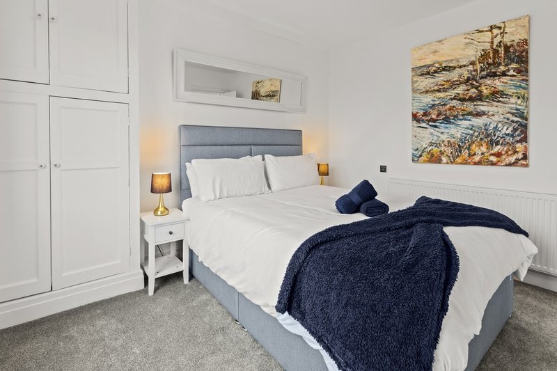 Modern bedroom with double bed, white wardrobes, bedside tables and coastal artwork