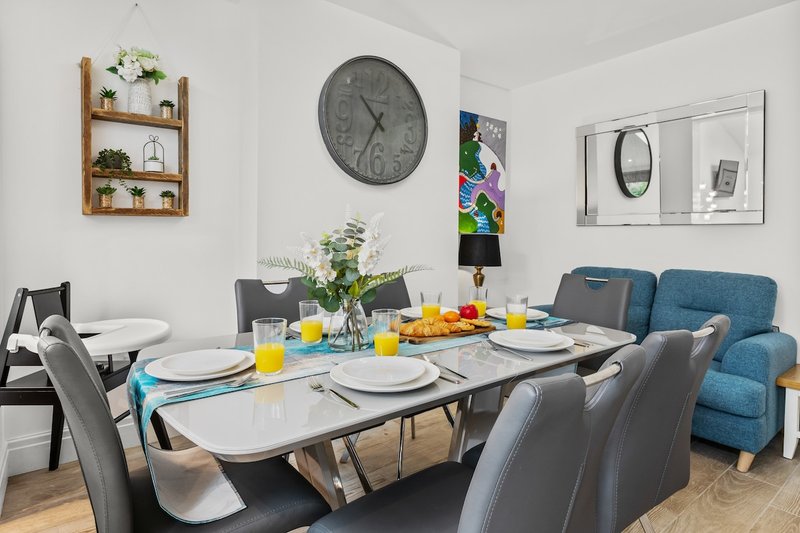 Dining room with white table, grey chairs, blue sofa, wall shelves and decorative items