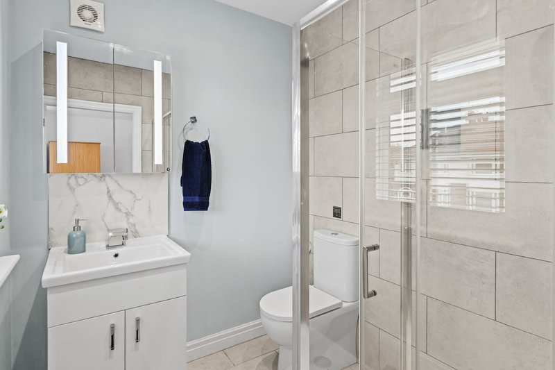 Modern bathroom with white vanity, illuminated mirror, walk-in shower enclosure and toilet