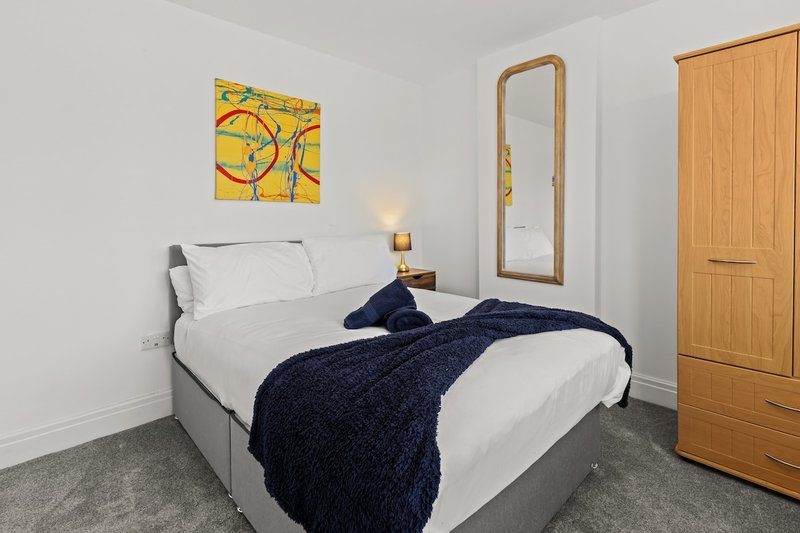 Bedroom with double bed, white bedding, dark blue throw, wooden wardrobe and mirror