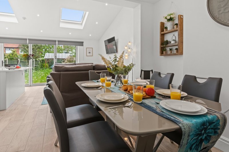 Modern dining room with table set for meal, black chairs, brown sofa, and garden view through large windows