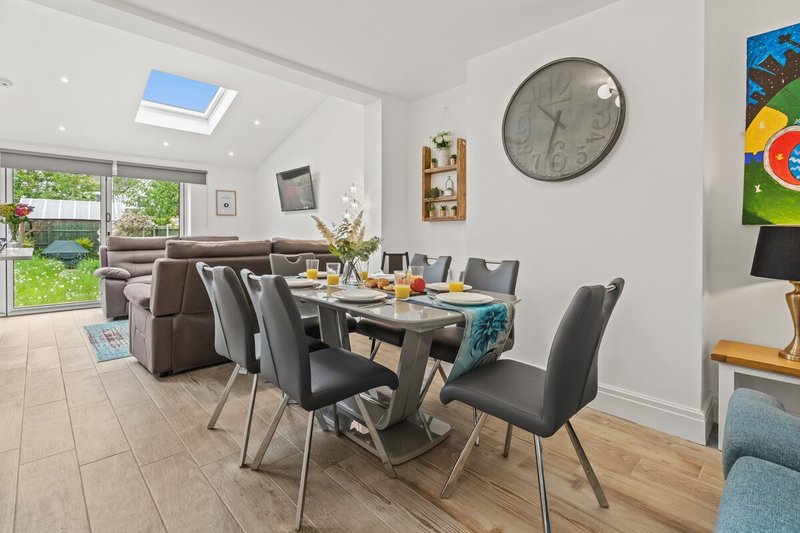 Open-plan dining and living area with table, chairs, sofa, wall clock and garden views