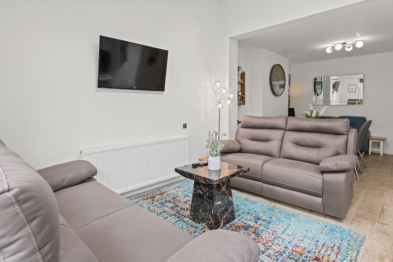 Modern open-plan living room with grey sofas, wall-mounted TV, marble table and kitchen visible beyond