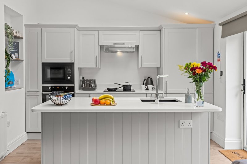 Modern white kitchen with island, built-in appliances, fresh flowers and fruit bowl