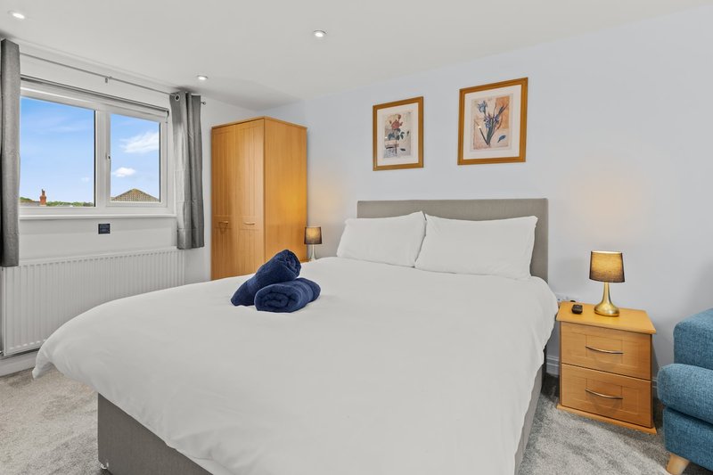Bright bedroom with double bed, wooden wardrobe, nightstand, and framed artwork on walls