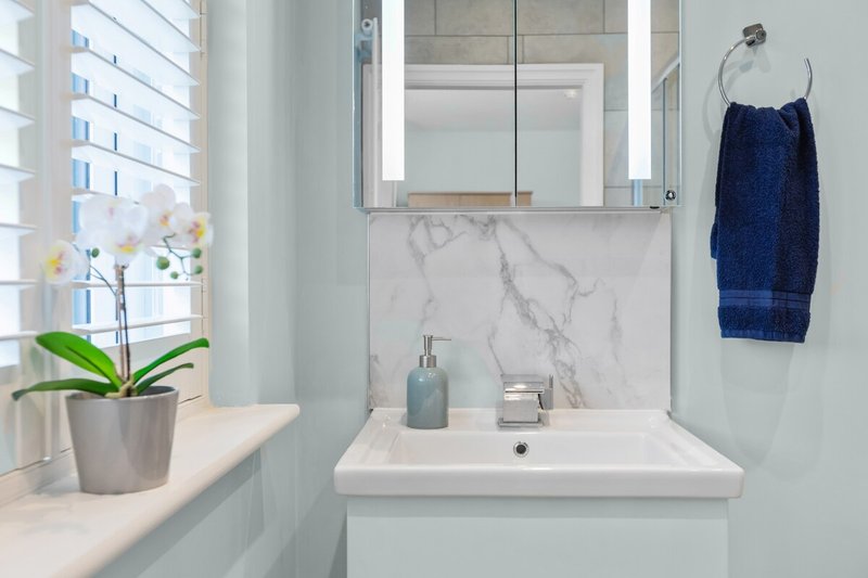 Modern bathroom with white sink, marble backsplash, mirror, plant, and towel rail